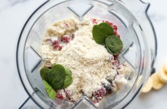 Overhead view looking down into a blender container with vanilla protein powder, berries and a few spinach leaves.